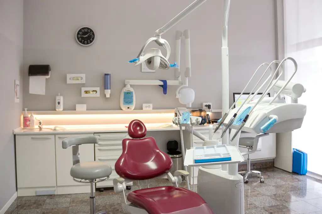 Treatment room with a red dental chair, sink and cabinets